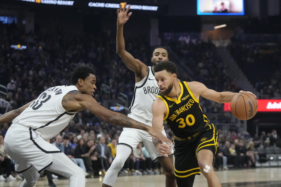Golden State Warriors guard Stephen Curry (30) drives to the basket against Brooklyn Nets center Nic Claxton, left, and forward Mikal Bridges during the first half of an NBA basketball game in San Francisco, Saturday, Dec. 16, 2023. (AP Photo/Jeff Chiu)