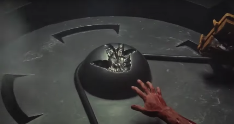 A man reaches for a metal orb with a handprint on it