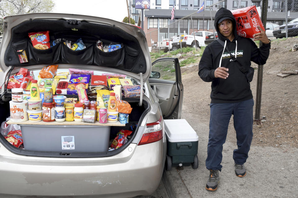 Alvaro Machado sells packaged food brands from South America out of the back of his car outside a motel designated for migrants in Denver, Colorado, Thursday, April 18, 2024. Machado, from Venezuela, said he came to Denver six months ago. (AP Photo/Thomas Peipert)