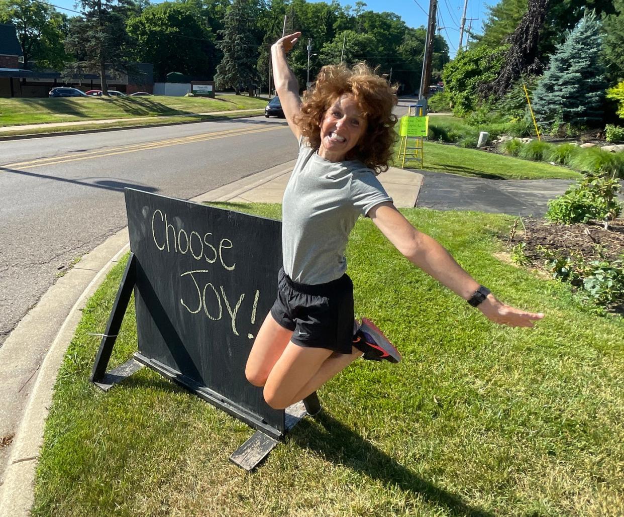 Jonna Siano jumps for joy beside her chalkboard sign along Capital Avenue Southwest on Thursday, June 30, 2022. Siano started writing daily messages of positivity on the sign when the pandemic began in 2020.