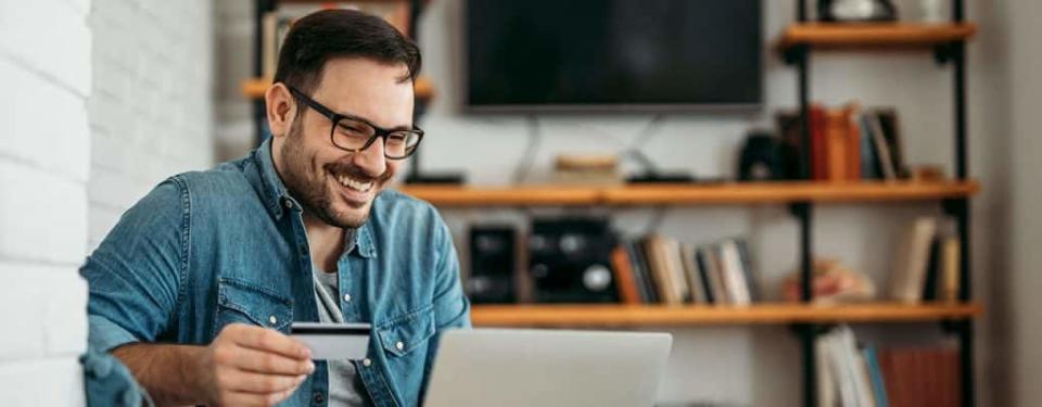 Man sitting on couch online shopping holding credit card wearing glasses slickdeals inbody