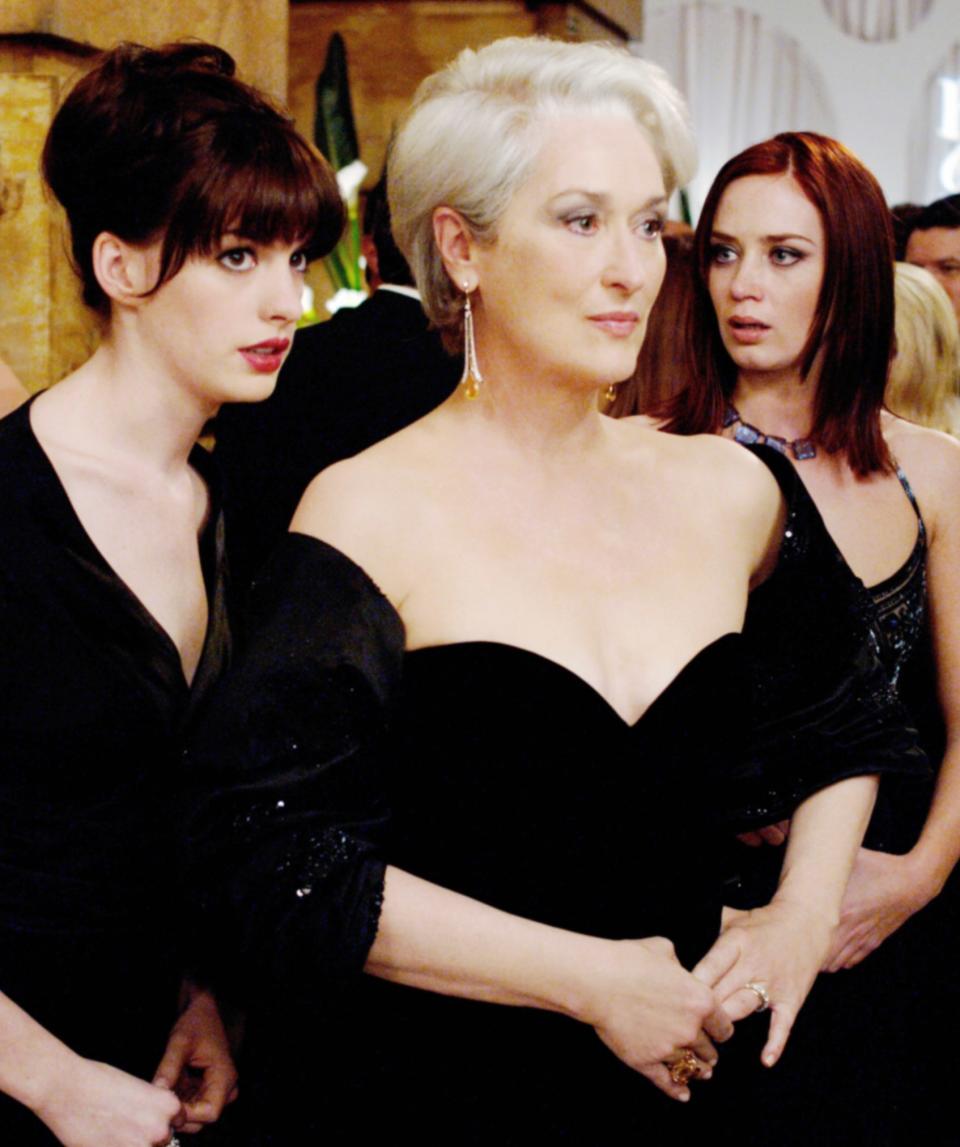 Anne Hathaway and Emily Blunt stand behind Meryl at a formal event in a scene from "The Devil Wears Prada"