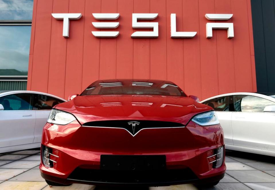 Red Tesla car with two white Teslas behind