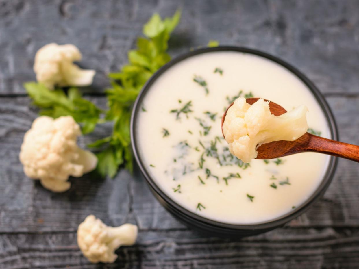 Spoon with a piece of cauliflower over a bowl of cream soup. Keto diet dish.