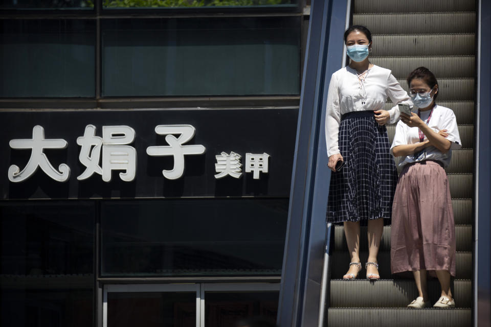 People wearing face masks to protect against the coronavirus ride an escalator past a sign of a nail salon at a shopping and office complex in Beijing, Tuesday, Aug. 11, 2020. Mainland China and semi-autonomous Hong Kong saw declines in their recent outbreaks Tuesday. (AP Photo/Mark Schiefelbein)