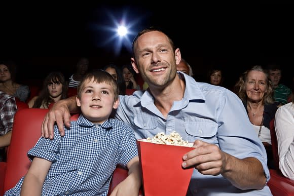 a father and son watch a movie in a theater with popcorn.