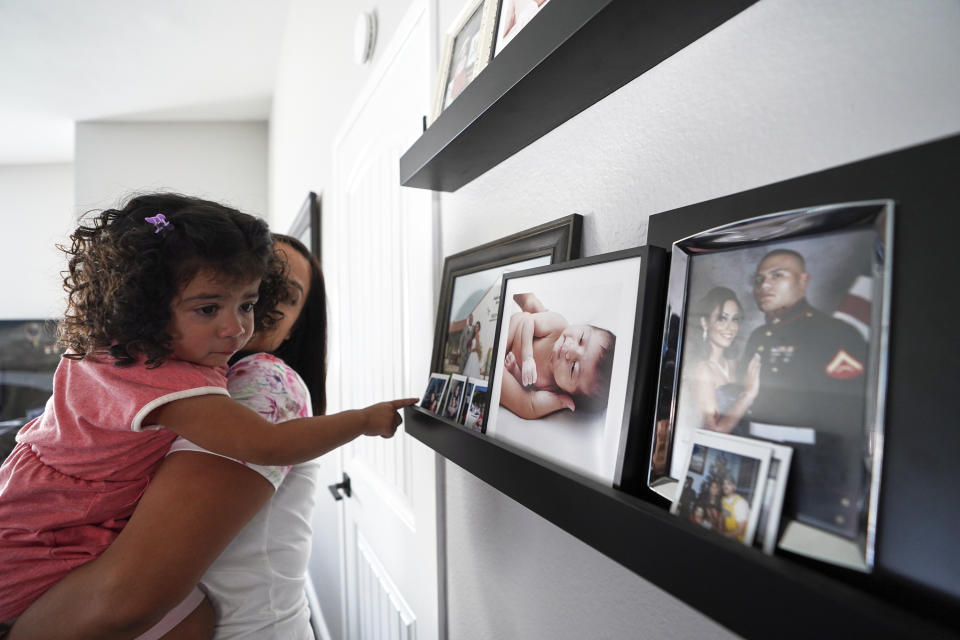 Laura Guerra and her daughter Emilia, 2, look at her father's pictures at their home in Riverside, Calif., on Monday, July 11, 2022. Rigo Guerra passed away on Dec. 24, 2020, due to complications following a monthlong battle with COVID-19. California has approved trust funds for some children from low-income families who lost a parent or caregiver to COVID-19. The Legislature set aside $100 million in the state budget to put into trust funds. (AP Photo/Damian Dovarganes)