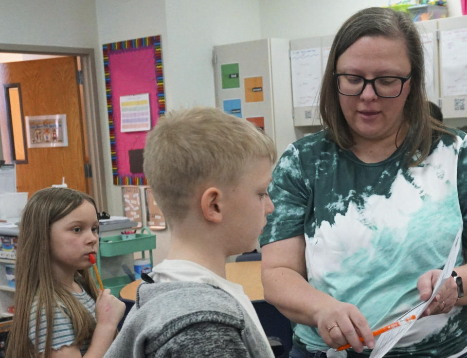 Erin Ulibarri, a third grade teacher at Endeavor Elementary, helps a student on Feb. 29, 2024, in Nampa, Idaho. Her son Theo, 1, attends the onsite daycare, which is more affordable than most in the area. (Carly Flandro/Idaho Education News via AP)