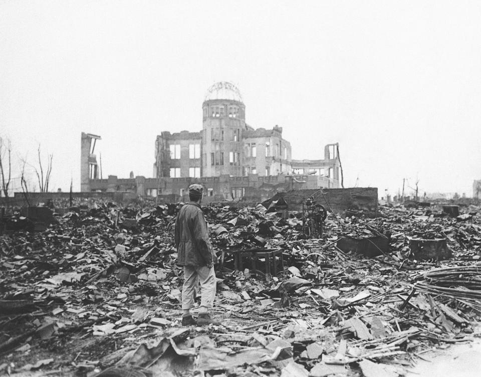 FILE - In this 1945 file photo, an Allied war correspondent stands in the ruins of Hiroshima, Japan, just weeks after the city was leveled by an atomic bomb. Many residents of Hiroshima welcome attention to their city from abroad, which IOC President Thomas Bach will bring when he visits on Friday, July 16. But Bach will also bring political baggage — as will his vice president John Coates when he visits Nagasaki the same day — that is largely unwelcome in two cities viewed as sacred by many Japanese. (AP Photo/File)