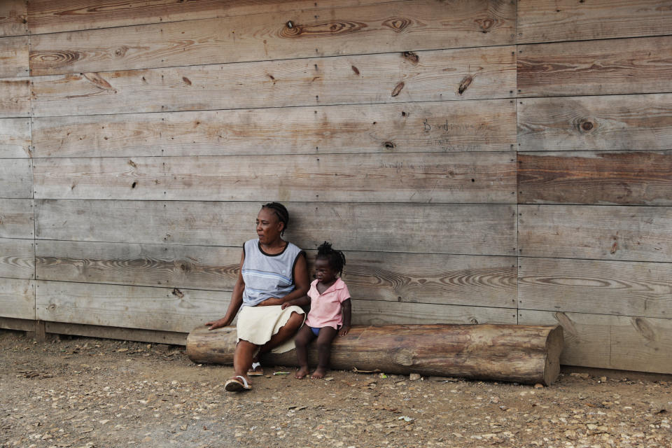 Duperat Laurette sits on a log with a girl at the entrance of a migrant shelter in Lajas Blancas, Darien province, Panama, Saturday, Aug. 29, 2020. The 45-year-old Haitian migrant and her husband emerged from the thick jungle that blankets the Panama-Colombia border here in Darien seven months earlier and have advanced no farther because of the new coronavirus pandemic. (AP Photo/Arnulfo Franco)