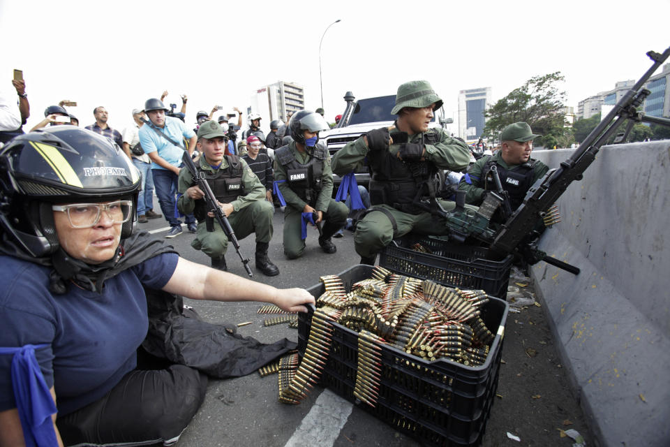 FILE - In this April 30, 2019 file photo, an anti-government protester sits by ammunition being used by rebel troops rising up against the government of Venezuela's President Nicolas Maduro as they all take cover on an overpass outside La Carlota military airbase where the rebel soldiers confront loyal troops inside the base in Caracas, Venezuela. Last April, as a military uprising roiled Venezuela, President Nicolás Maduro’s socialist government ordered pay TV providers to immediately cease transmission of CNN and the BBC. DirecTV, which is wholly owned by AT&T, quickly obliged, yanking the two networks off the air. (AP Photo/Boris Vergara, File)
