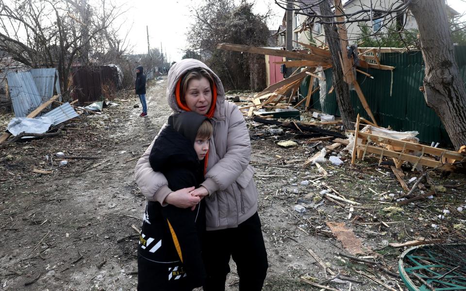 Local residents stand among debris on the street outside a house destroyed as a result of a drone attack in Tairove