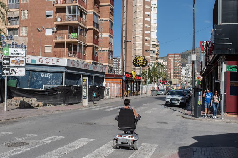 A woman rides her mobility scooter slowly past a closed bar on May 11, 2020 in Benidorm, Spain.