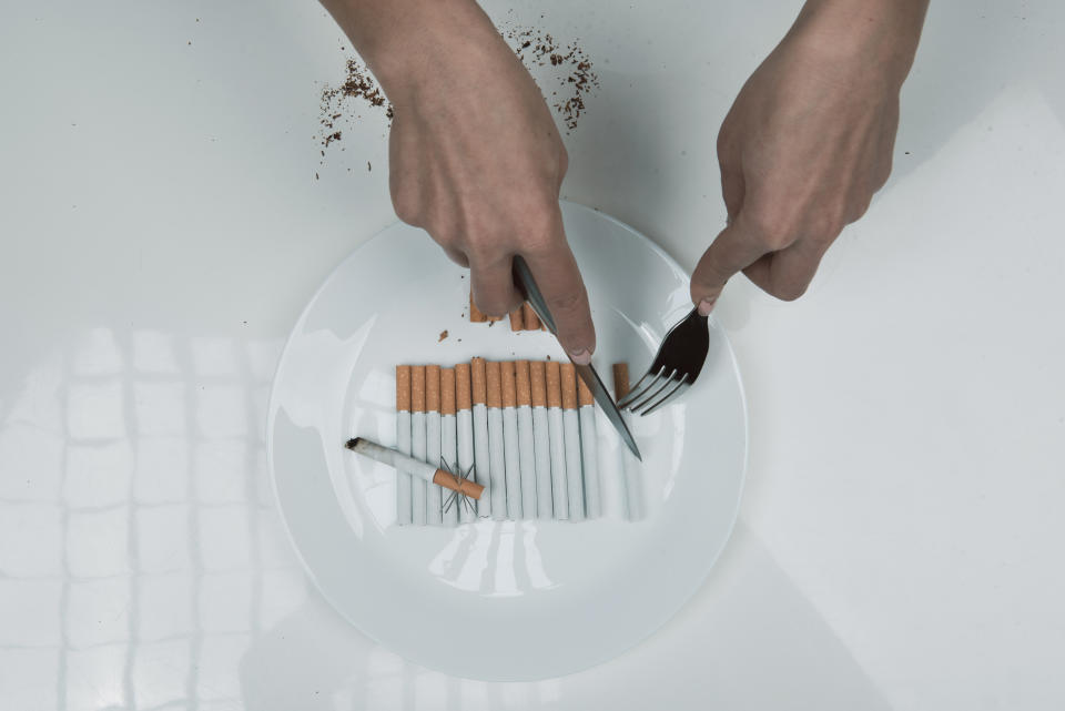 Top view close up of woman arms cutting ciggy that is lying in the plate with knife and fork