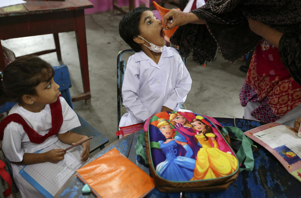 A health worker administers a polio vaccine to a child at a school in Lahore, Pakistan, Monday, Aug. 2, 2021. The government launched polio vaccination drives across Pakistan to hopefully eradicate the crippling disease by the end of the year. (AP Photo/K.M. Chaudhry)