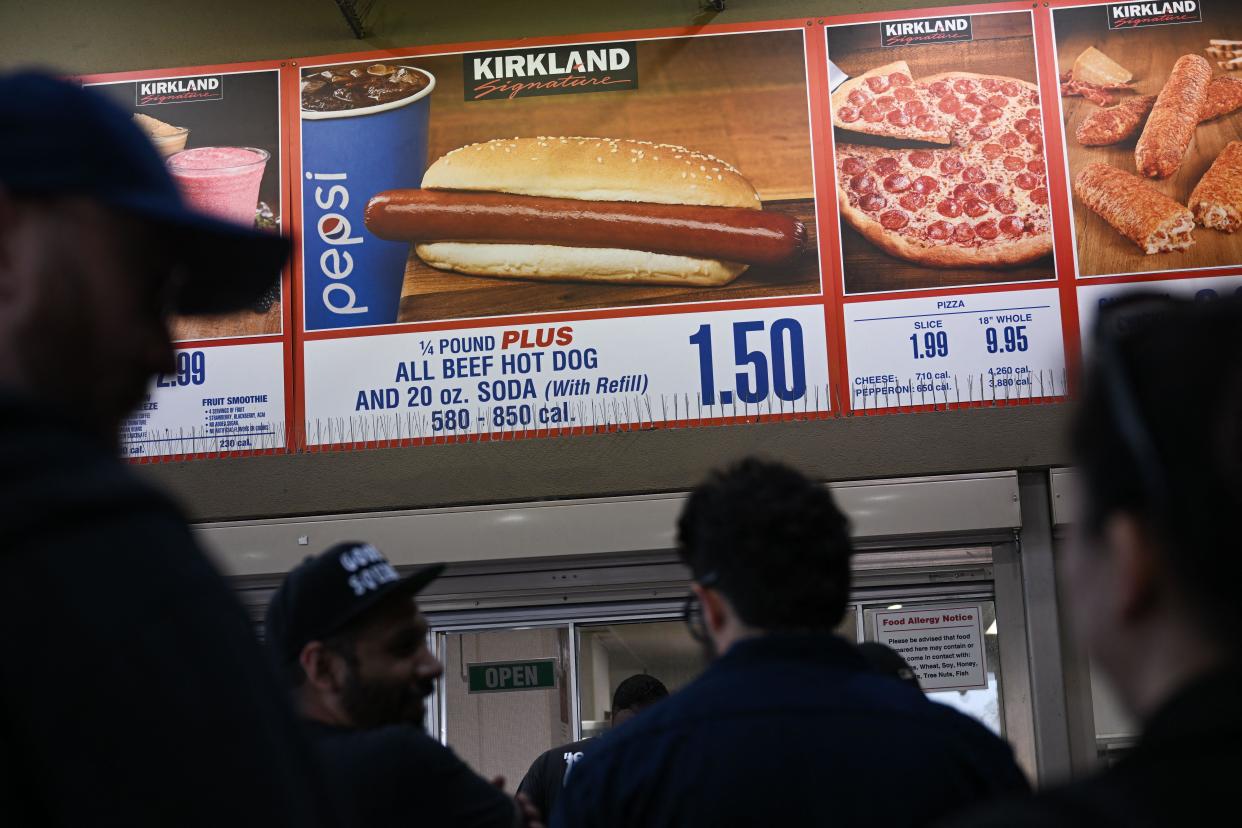 Customers wait in line to order below a sign for a $1.50 hot dog and soda combo at Costco.