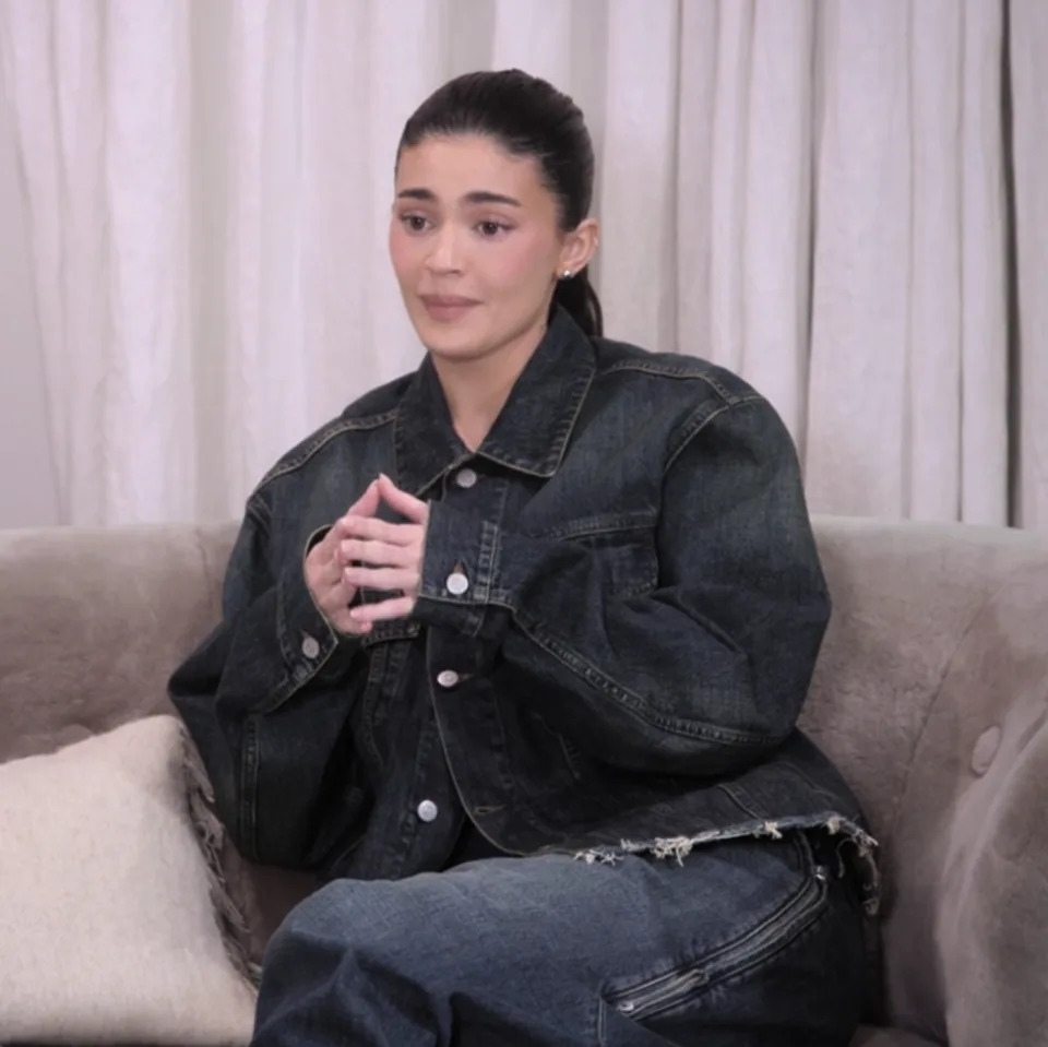 Kylie Jenner sentada en un sofá, vestida con una chaqueta vaquera de gran tamaño y jeans, dando una entrevista