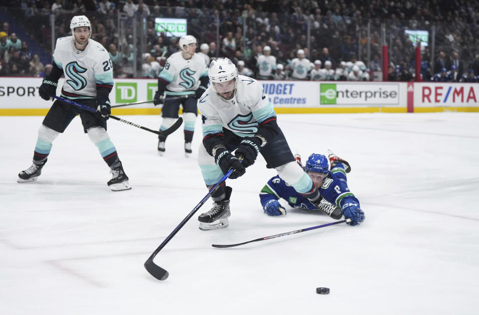 Seattle Kraken's Justin Schultz (4) and Vancouver Canucks' Brock Boeser (6) vie for the puck during the third period of an NHL hockey game Tuesday, April 4, 2023, in Vancouver, British Columbia. (Darryl Dyck/The Canadian Press via AP)