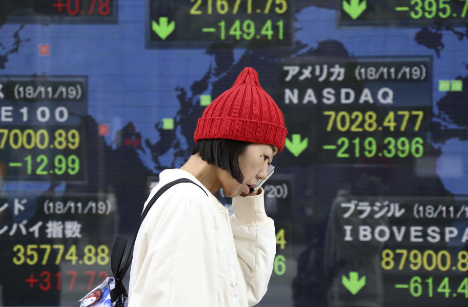 A woman walks by an electronic stock board of a securities firm in Tokyo, Tuesday, Nov. 20, 2018. Asian stocks slid Tuesday after tech losses dragged down Wall Street and Nissan's chairman was arrested on charges of financial misconduct. (AP Photo/Koji Sasahara)