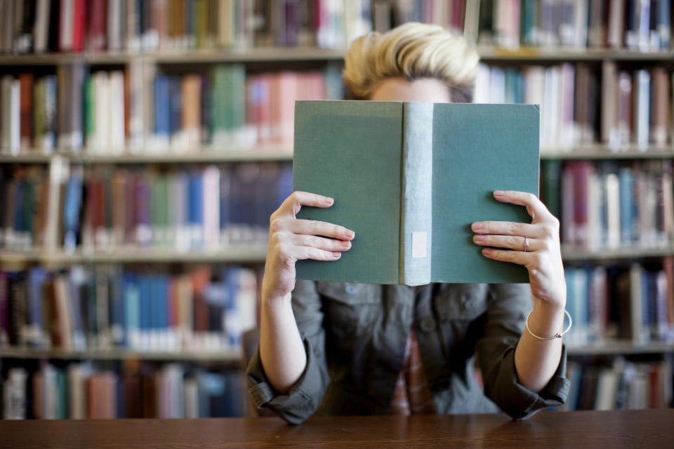 someone hiding their face behind a book at a library