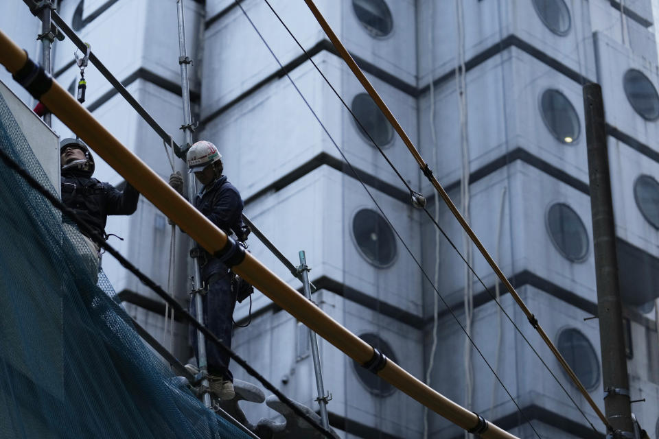 Men work at the site of the Nakagin Capsule Tower, a capsule hotel n the Ginza district, as parts of the hotel were being demolished, in Tokyo on April 7, 2022. It’s now being demolished in a careful process that includes preserving some of its 140 capsules, to be shipped to museums around the world. (AP Photo/Hiro Komae)