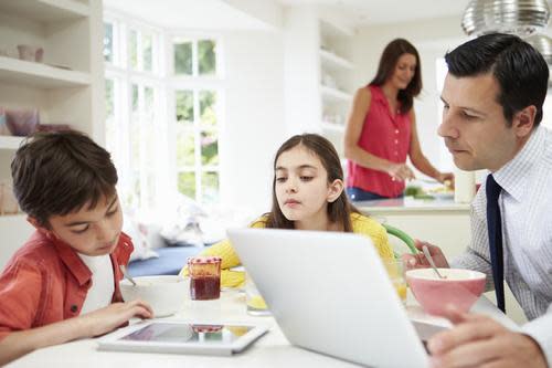 Family eating breakfast while looking at screens