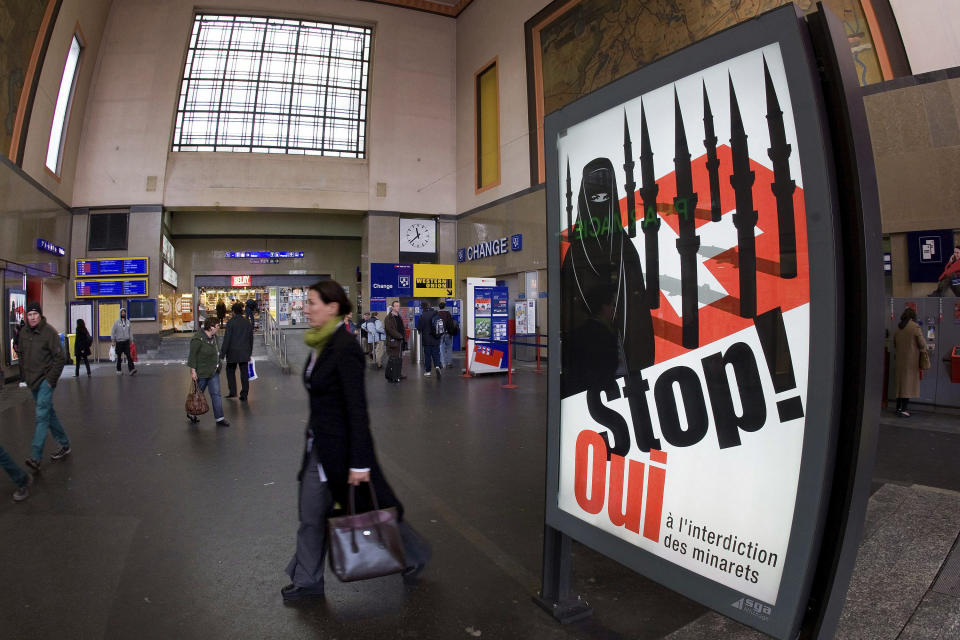 FILE - In this Nov. 4, 2009, file photo, people walk by a poster from the right-wing Swiss People's Party (SVP/UDC) depicting a woman wearing a burqa in front of a Swiss flag upon which are minarets which resemble missiles, at the central station in Geneva, Switzerland. Later in the month, a successful referendum banned the construction of new minarets in the country. (Salvatore Di Nolfi/Keystone via AP, File)