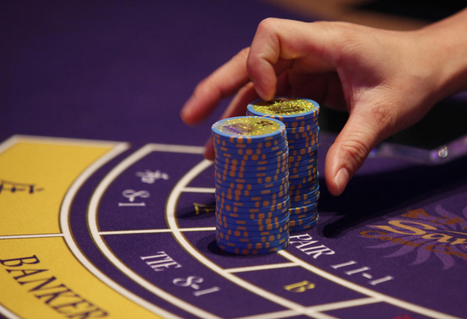 FILE - A croupier counts the chips at a baccarat gaming table inside a casino at the Sands Cotai Central in Macao, Sept. 20, 2012. The Asian gambling center of Macao will close all its casinos for a week starting Monday, July 11, and largely restrict people to their homes as it tries to stop a COVID-19 outbreak that has infected more than 1,400 people in the past three weeks. (AP Photo/Kin Cheung, File)