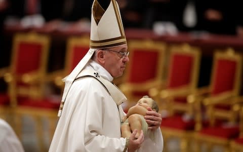 Pope Francis holding a statue of Baby Jesus leaves at the end of the Christmas Eve Mass celebrated in St. Peter's Basilica at the Vatican - Credit: AP
