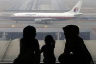 Dos mujeres y una niña miran a un avión de Malaysia Airline en la pista del aeropuerto de Kuala Lumpur este 13 de marzo de 2014, a seis días de la desaparición del vuelo MH370 sin dejar rastro. REUTERS/Damir Sagolj