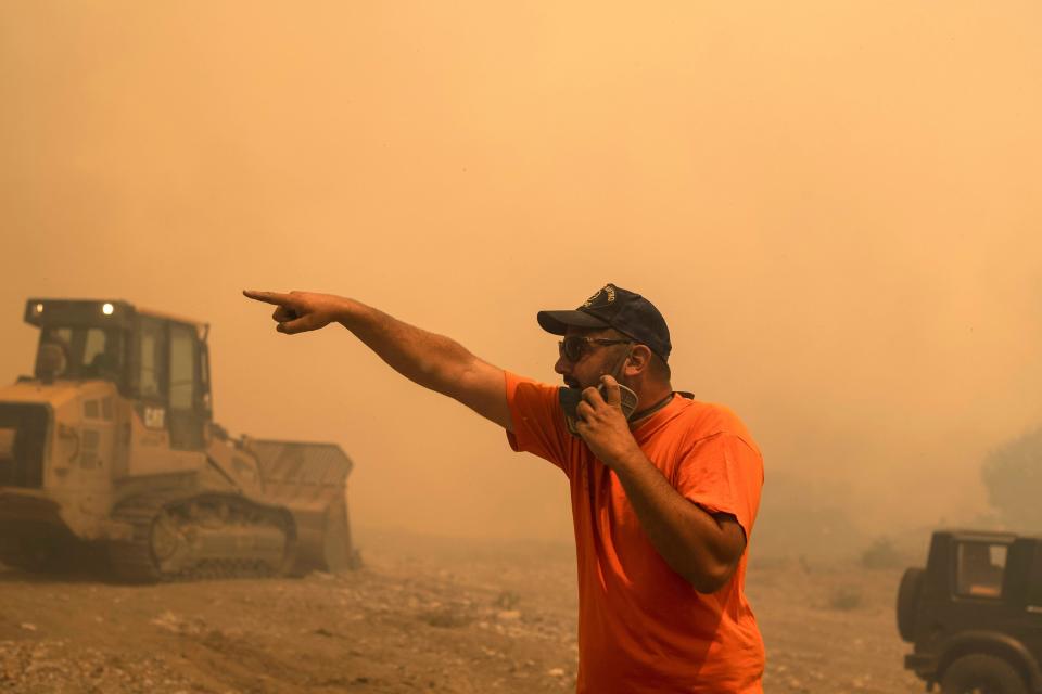 A volunteer gives directions during a wildfire in Vati village, on the Aegean Sea island of Rhodes, southeastern Greece, on Tuesday, July 25, 2023. A third successive heat wave in Greece pushed temperatures back above 40 degrees Celsius (104 degrees Fahrenheit) across parts of the country Tuesday following more nighttime evacuations from fires that have raged out of control for days. (AP Photo/Petros Giannakouris)