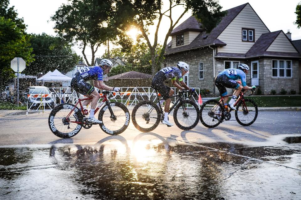 A group of riders passes a sprinkler set up at the corner of S. 68th Street and W. Rogers Street during the West Allis Cheese Wheel Classic on Tuesday, June 21, 2022,i n West Allis, Wisconsin. The event marked the sixth day of the Tour of America's Dairyland cycling series. The temperature at the start of the race was nearly 100 degrees.