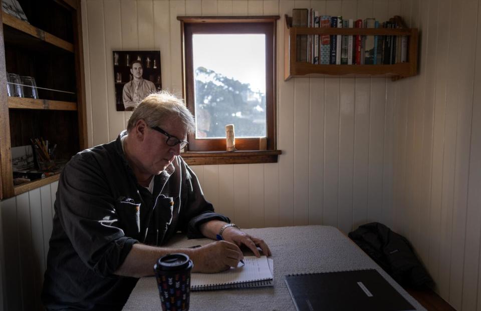 A man, writing, sits at a table aboard a boat.