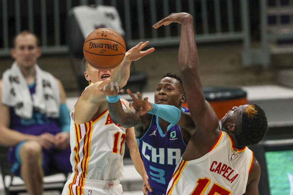 Charlotte Hornets guard Terry Rozier, center, passes between Atlanta Hawks guard Bogdan Bogdanovic, left, and center Clint Capela, right, during the second quarter of an NBA basketball game in Charlotte, N.C., Sunday, April 11, 2021. (AP Photo/Nell Redmond)
