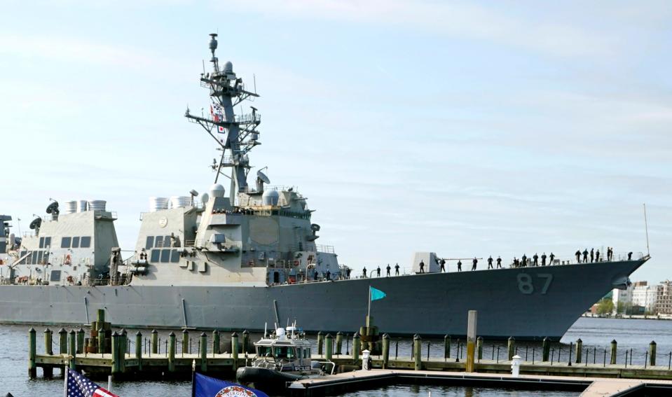 Destroyer USS Mason sails past a dock with a police vessel parked nearby.