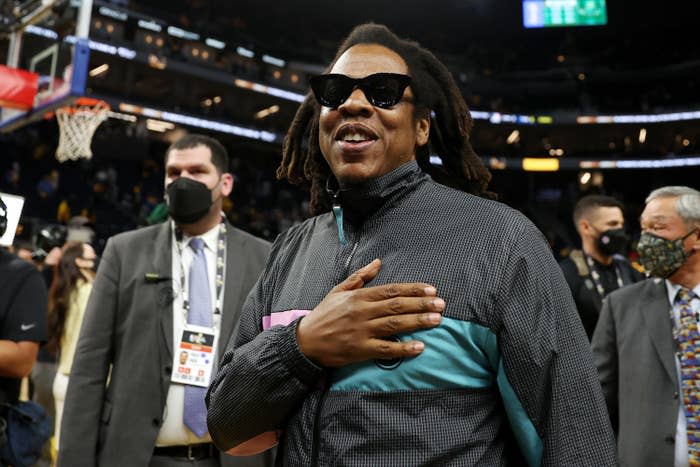 Jay-Z smiling with his hand on his heart at a basketball game