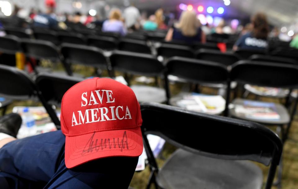 A person with a red cap that says "Save America" and an autograph on its bill