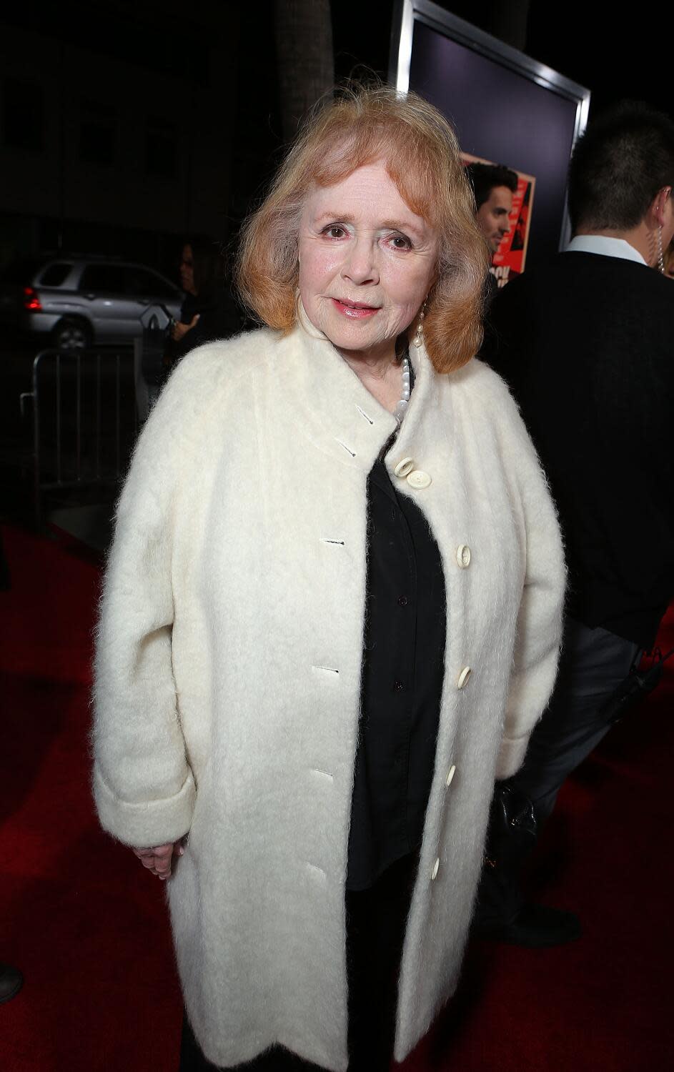 A woman with red hair in a white coat over a black dress.