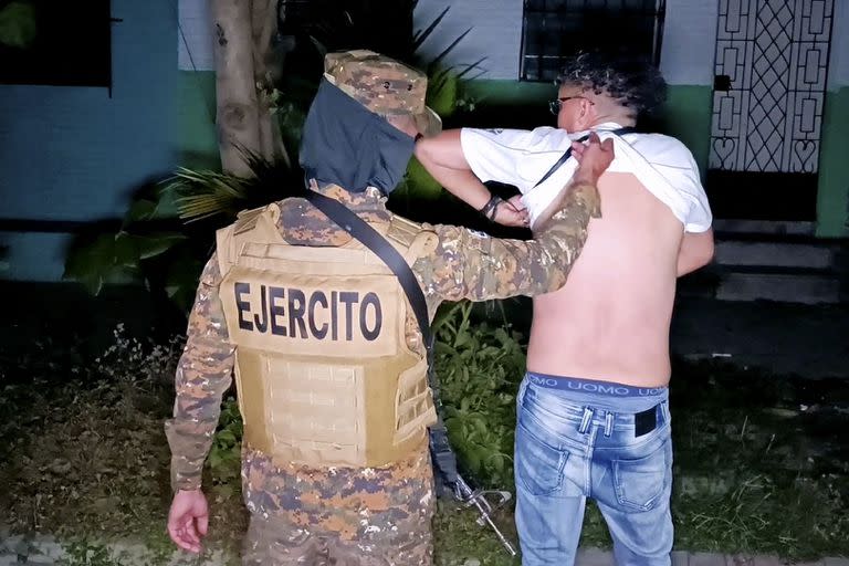 Una imagen difundida por la oficina de prensa de la Presidencia de El Salvador muestra a un soldado revisando el cuerpo de un hombre en busca de tatuajes durante una operación de búsqueda de pandilleros en Soyapango, El Salvador, el 3 de diciembre de 2022.