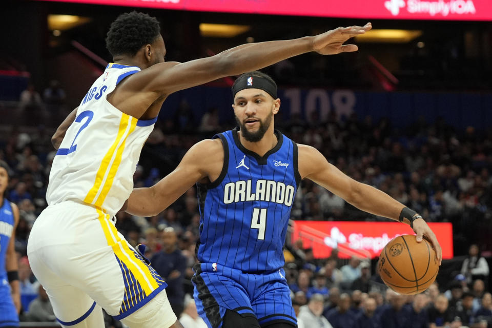 Golden State Warriors forward Andrew Wiggins, left, blocks the path of Orlando Magic guard Jalen Suggs to the basket during the first half of an NBA basketball game Wednesday, March 27, 2024, in Orlando, Fla. (AP Photo/John Raoux)