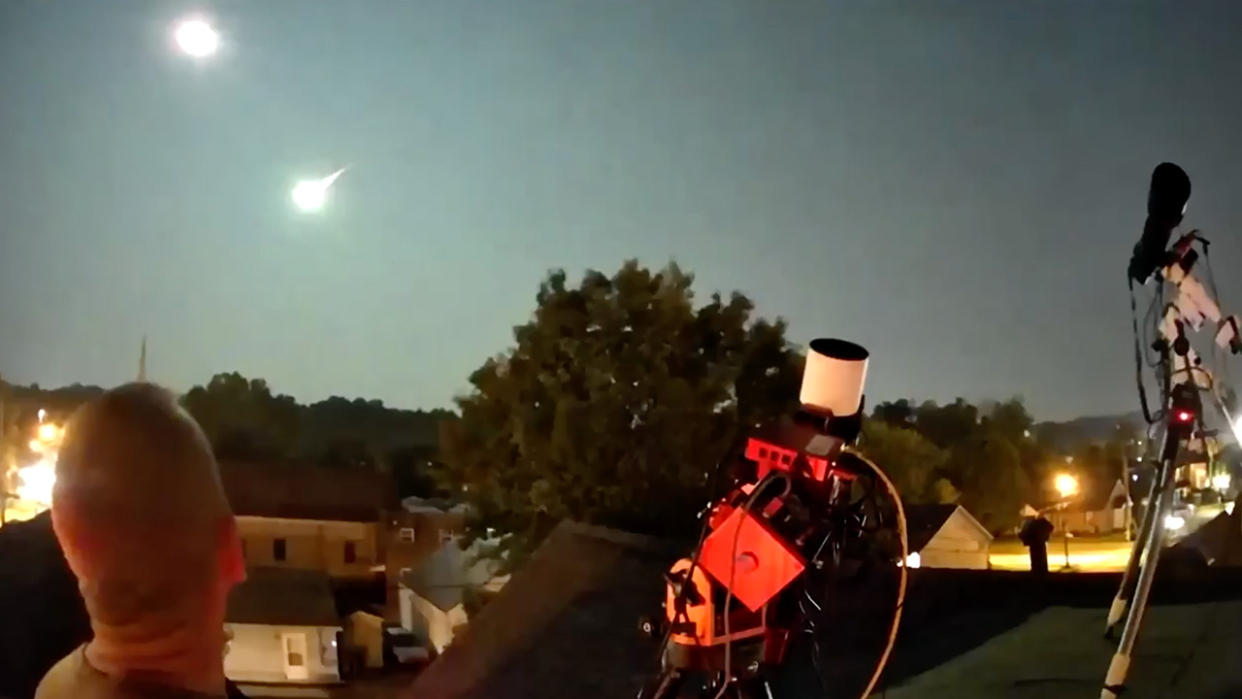  a fireball streaks through the sky while people below watch 