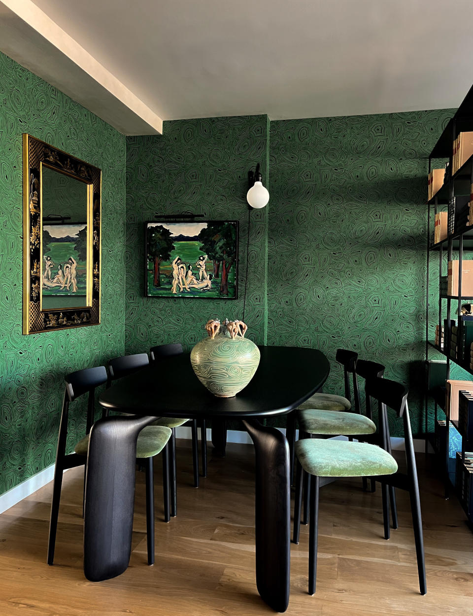 A dining room with a green wallpaper and black dining table and chairs