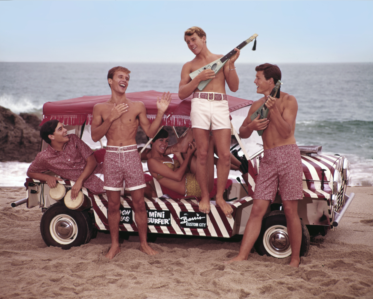Four guys and a girl, all students, sit or stand next to a Barris surf car, while wearing the latest fashion in Jantzen bathing suits, California, 1966