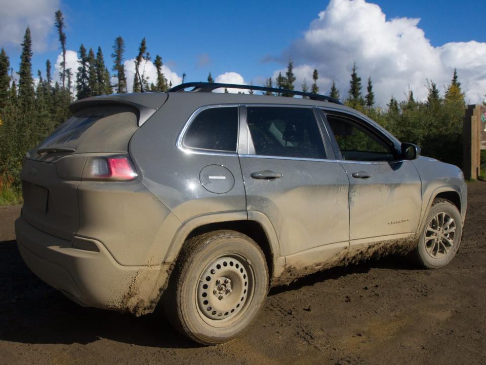 A dirty muddy car parked next to pine trees.