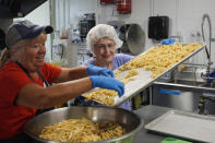 Glori Stauch, left, and Sally Young prepare a vegetable and pasta salad for clients at House of Hope, Tuesday, May 21, 2024, in Stuart, Fla. House of Hope and other nonprofits will make available packages of foods and other items to their clients before a storm impacts their area. House of Hope provides food, clothing for people in need as well as enrichment programs for all ages. (AP Photo/Marta Lavandier)