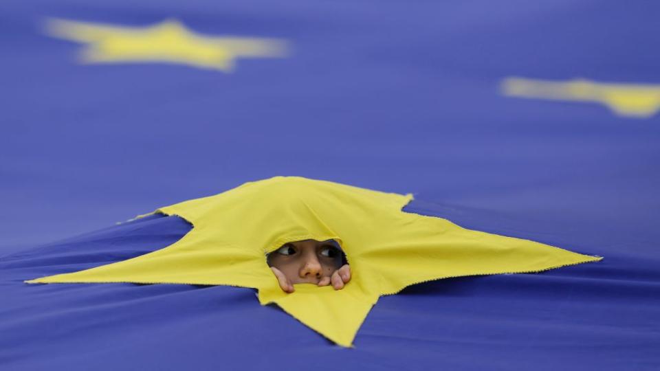 child peers through hole in start of european union flag