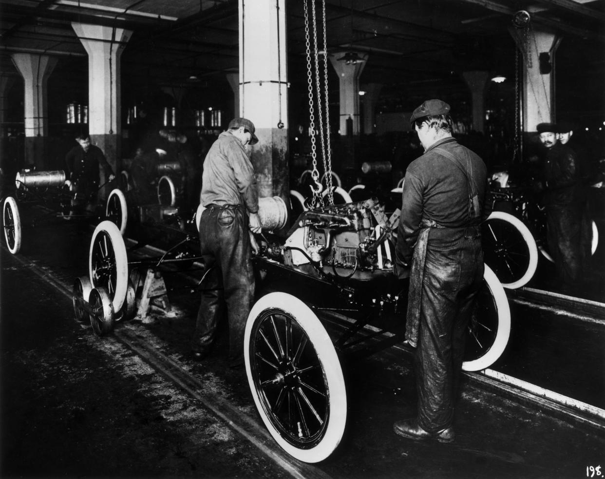 1914: Workers constructing a Model-T engine on an assembly line in a Ford Motor Company factory.