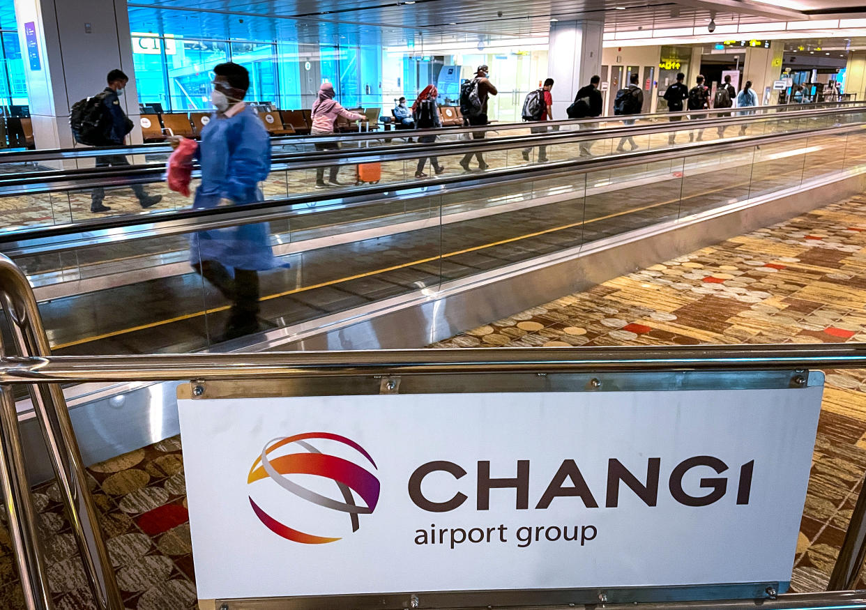 A member of staff wearing protective clothing and a face mask walks in front of passengers walking in a single line towards their boarding gate at Changi International Airport on 14 July 2021 in Singapore. (Photo by David Gray/Getty Images)