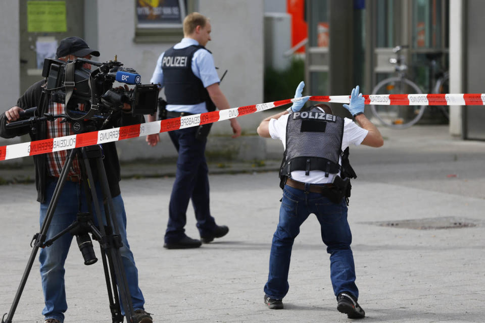 A cameraman films at the scene of a stabbing next to police officers at a station in Grafing near Munich, Germany, Tuesday, May 10, 2016. (AP Photo/Matthias Schrader)
