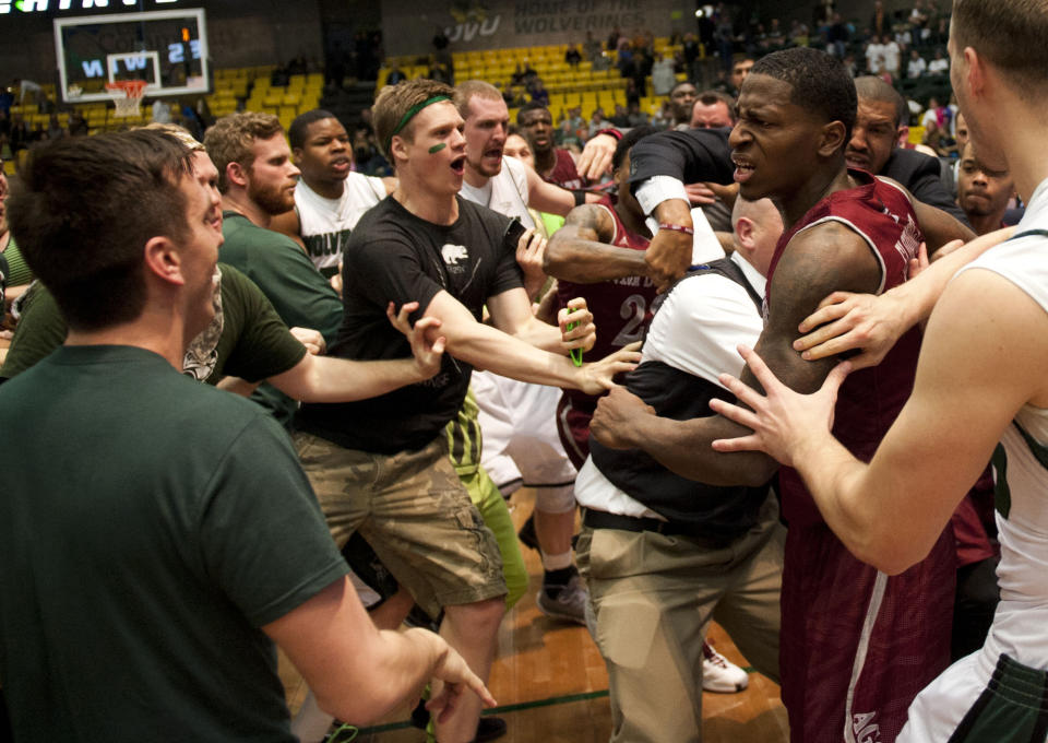 In this Thursday, Feb. 27, 2014 photo, New Mexico State's DK Eldridge, at right in red and white uniform, is held by security during a brawl involving players and fans who came onto the court when New Mexico State guard K.C. Ross-Miller hurled the ball at Utah Valley's Holton Hunsaker seconds after the Wolverines' 66-61 overtime victory against the Aggies in Orem, Utah. (AP Photo/The Daily Herald, Grant Hindsley) MANDATORY CREDIT